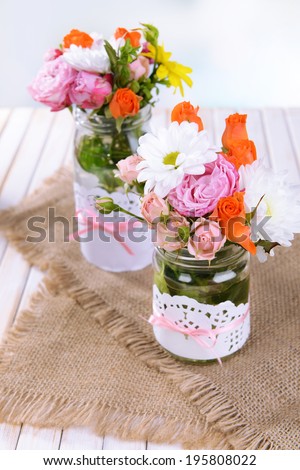 Beautiful bouquet of bright flowers in jars on table on light background