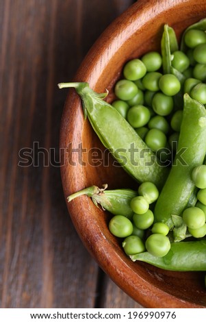 Green peas in wooden bowl on wooden background