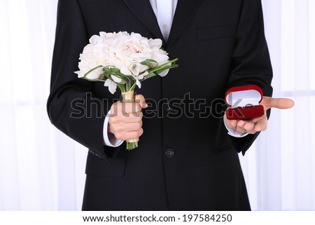 Man holding wedding bouquet and rings on light background