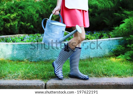 Young woman in rubber boots holding watering can, outdoors