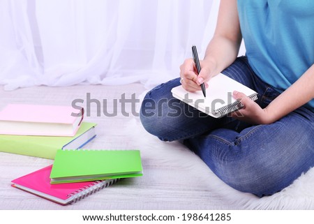 Closeup of young female student sitting on floor and studying, on light background