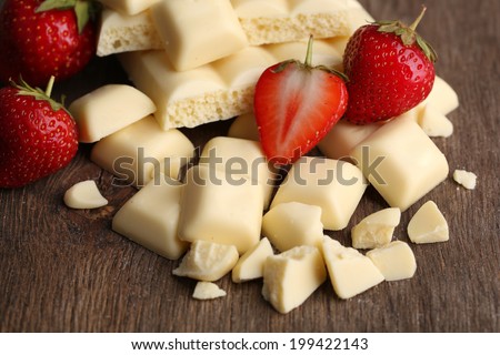 Broken white chocolate bar with fresh strawberries, on color wooden background