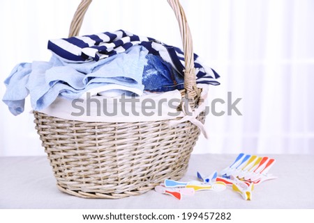 Colorful clothes in basket and pins on table, on light background