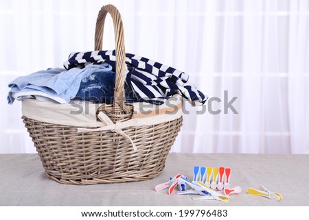 Colorful clothes in basket and pins on table, on light background