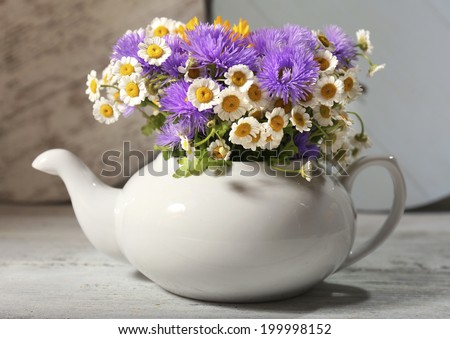 Kitchen decoration with teapot and wild flowers on wooden background