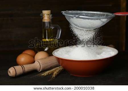 Sifting flour into bowl on table on wooden background
