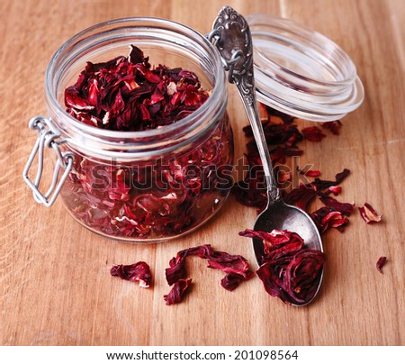 Dried hibiscus tea in glass jar on wooden background