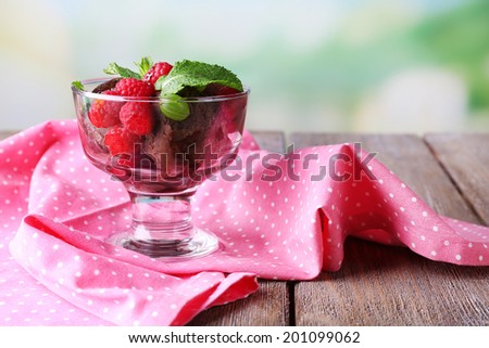 Chocolate ice cream with mint leaf and ripe berries in glass bowl, on  wooden  table, on bright background