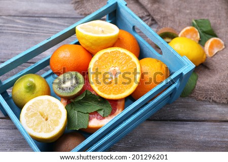 Fresh exotic fruits with green leaves in wooden box on color wooden background