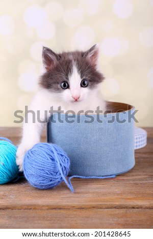 Cute little kitten in box playing with thread ball, on light background