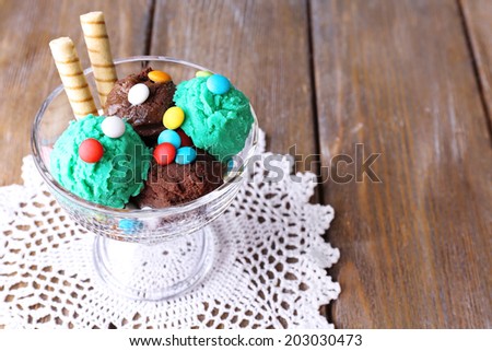 Chocolate ice cream with multicolor candies and wafer rolls in glass bowl, on wooden background