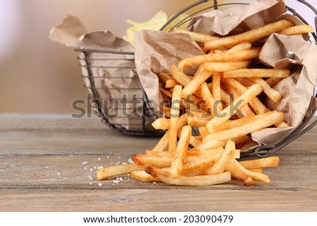 Tasty french fries and potato chips in metal baskets on wooden table, on light background