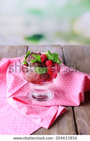 Chocolate ice cream with mint leaf and ripe berries in glass bowl, on  wooden  table, on bright background