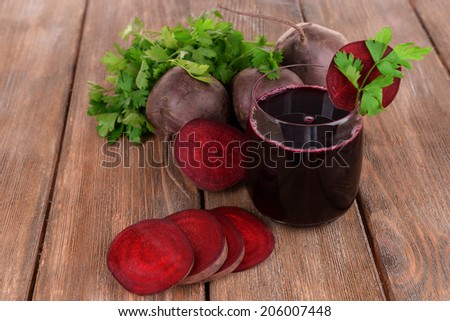 Glass of fresh beet juice and vegetables on wooden background