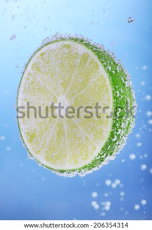 Fresh lime in water with bubbles on blue background