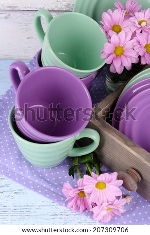 Bright dishes with flowers in crate on wooden background