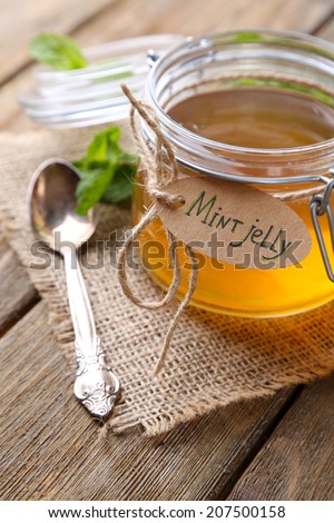 Homemade mint jelly in glass jar, on wooden background