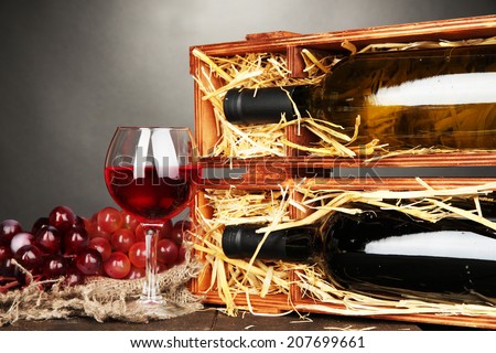 Wooden case with wine bottles, wineglass and grape on grey background