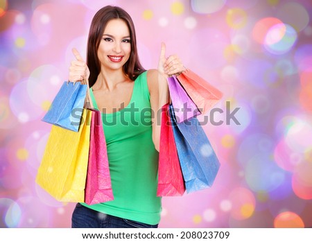 Beautiful young woman with gift bags on bright background