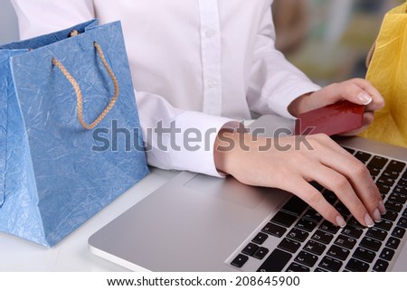 Female hands holding credit card with laptop and paper bags on table on bright background