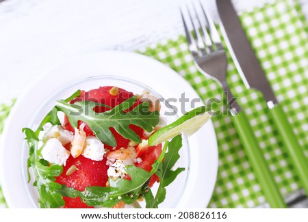 Salad with watermelon, feta, arugula shrimps, balsamic sauce in cocktail glass, on wooden background