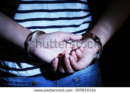 Criminal hands locked in handcuffs on dark background