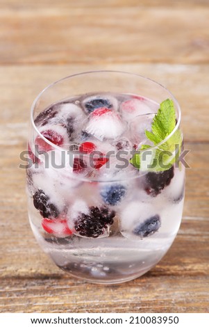 Cold cocktail with forest berries, frozen in ice cubes on wooden background