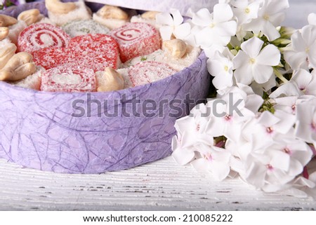 Present box with sweets and flowers on wooden background
