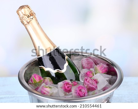 Frozen rose flowers in ice cubes and champagne bottle in bucket, on light background
