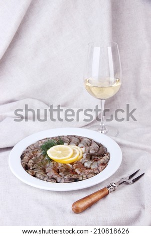 White round plate of prawns with dill and lemon and a glass of wine on white tablecloth