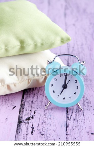 Plastic clock on a silk pillows on wooden purple background