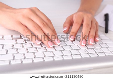 Female hands typing on keyboard, close-up, on dark background
