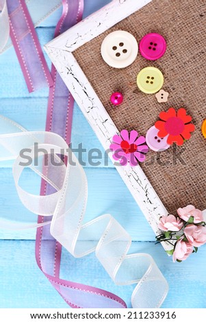 Scrapbooking craft materials and wooden frame with sackcloth inside on color wooden background
