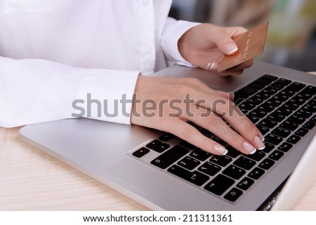 Female hands holding credit card and laptop on table on bright background
