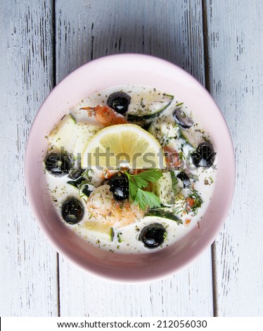 Fresh prawns with olives, lemon and parsley in white sauce on pink round plate on grey wooden background