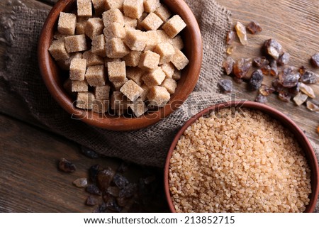 Brown sugar cubes, reed and crystal sugar in bowl on wooden background
