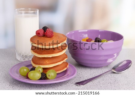 Pancake with berries and muesli with milk on table on bright background