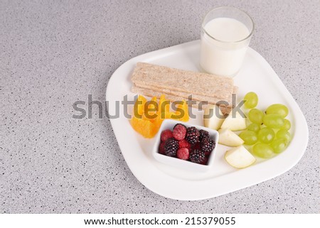 Slices of fruits with crispbreads and glass of milk on plate on table close up