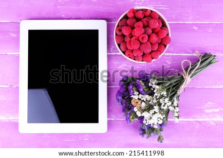 Tablet, field flowers and bowl of raspberries on wooden background