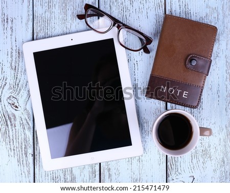 Tablet, mug of coffee, notebook and glasses on wooden background