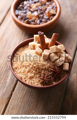 Brown sugar cubes and crystal sugar with spices in bowl on wooden background