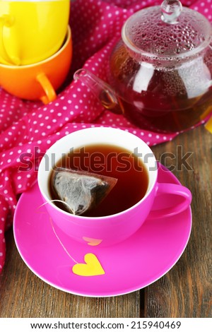 Cup of tea, teapot and tea bags on wooden table close-up