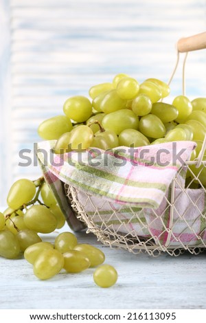 Ripe grapes in metal basket with napkin on wooden table on light background