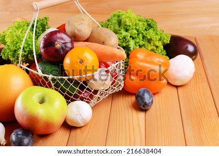Fresh organic fruits and vegetables in wicker basket on wooden background