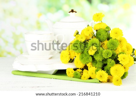 Bouquet of flowers, teapot and cup on wooden table, on bright background