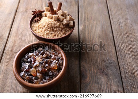 Brown sugar cubes, reed and crystal sugar in bowls on wooden background