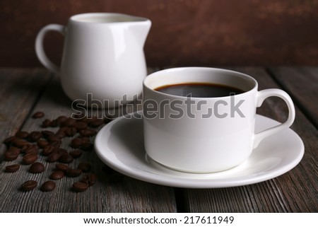 Cup of coffee with cream in milk jug and coffee beans on wooden table on dark background
