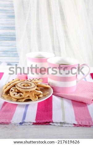 Two mugs of coffee with biscuits on napkin on table on white curtain background