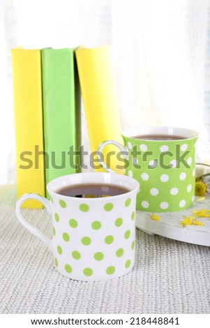 Two cups of tea and books on table on curtain background