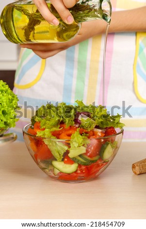 Woman pouring olive oil in vegetable salad in kitchen
